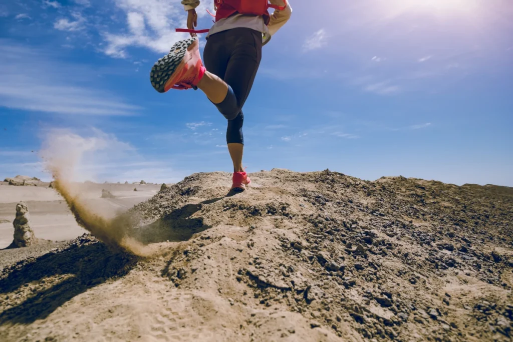 Une coureuse en legging noir et baskets roses accélérant sur une colline aride, soulignant l'importance des leggings pour le soutien musculaire et la mobilité pendant la course